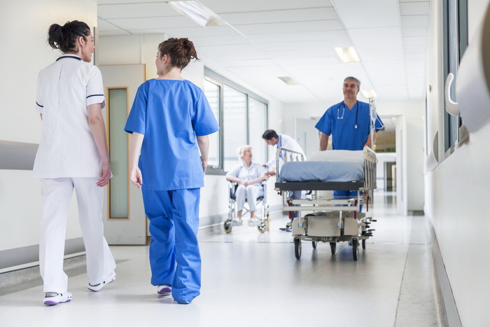 Male nurse pushing stretcher gurney bed in hospital corridor with doctors & senior female patient